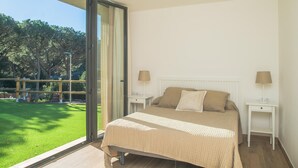 A bedroom with a large bed, two bedside tables, and a view of a grassy outdoor area through a sliding glass door.