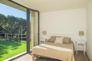 A bedroom with a large bed, two bedside tables, and a view of a grassy outdoor area through a sliding glass door.