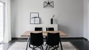 Ein stilvolles Esszimmer mit Holztisch, schwarzen Stühlen, einer schwarzen Pendelleuchte, gerahmten Kunstwerken und einer Vase mit Trockenblumen.