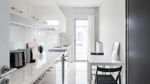 Eine moderne Küche mit weißen Schränken, einem Edelstahlkühlschrank, einem Esstisch mit zwei Stühlen und einem Fenster, das für natürliches Licht sorgt.
