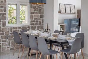 A dining area with a stone wall, a large window, and a modern chandelier. - Villa Collis-apartment with private heated pool! (Makarska)