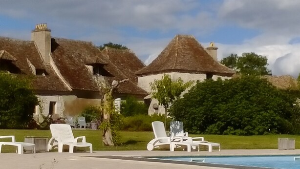 A pool area with lounge chairs, a thatched-roof building, and a clear sky. - Luxury gite for adult couples, peaceful, open views, large swimming pool (Boisse)