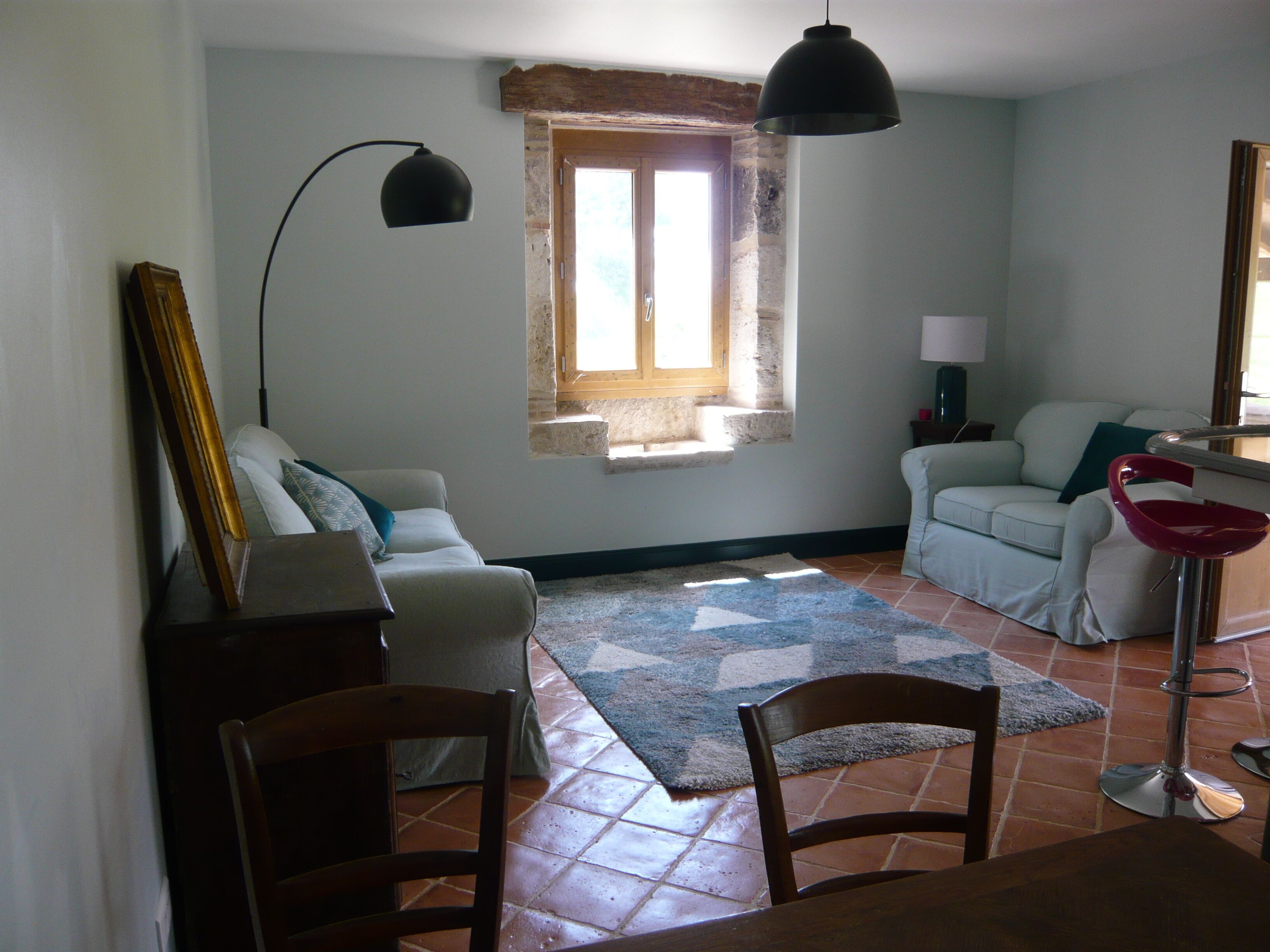 Een woonkamer met een bank, een stoel, een tafel, een lamp en een raam met uitzicht.