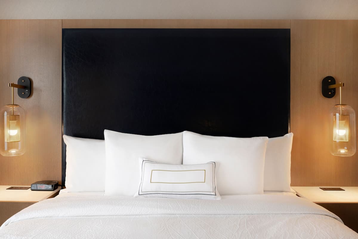 Una habitación de hotel con una cama grande, dos mesitas de noche y un cabecero oscuro.