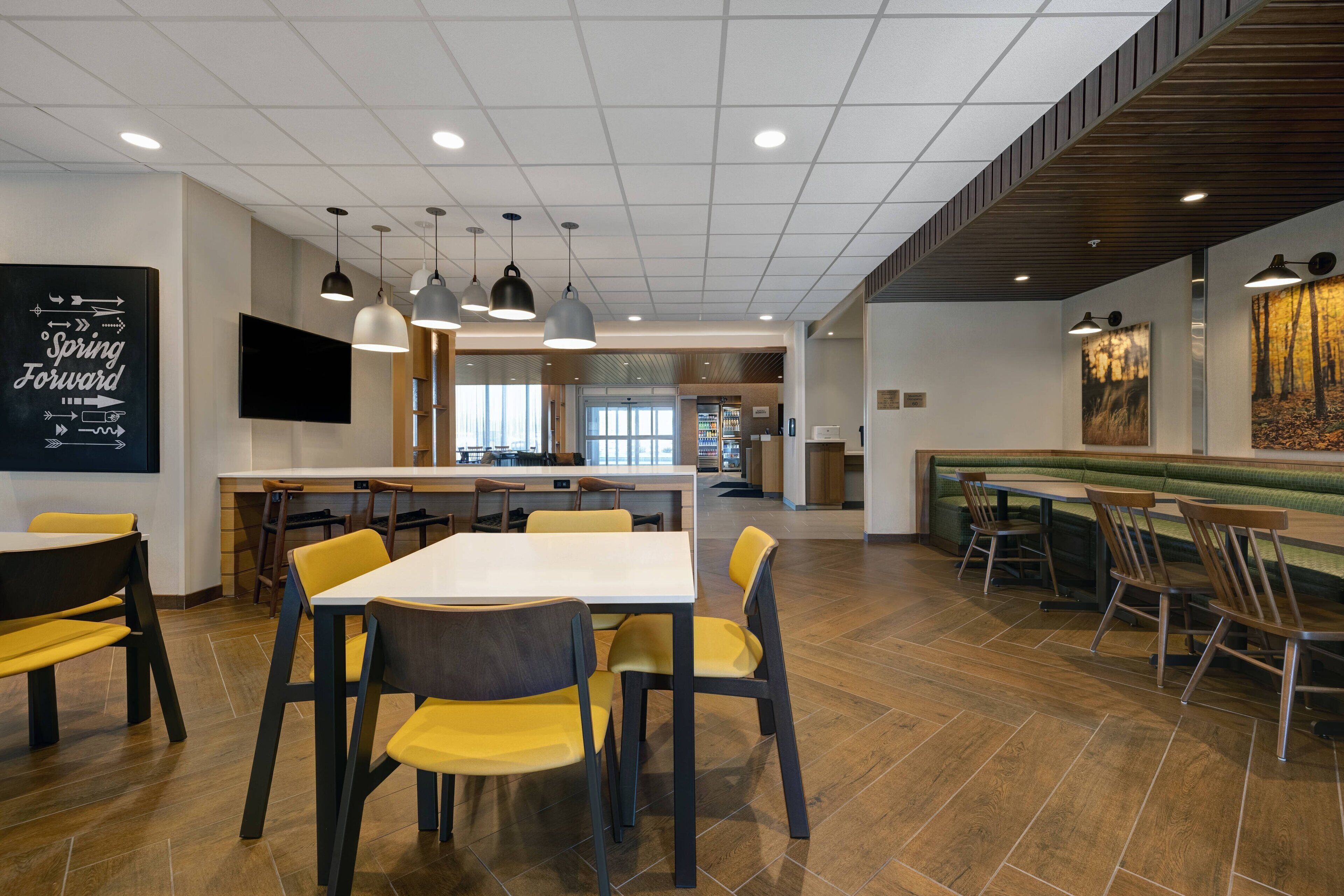 Un espace de repas moderne avec des tables et des chaises, une cuisine en arrière-plan et un grand tableau accroché au mur.
