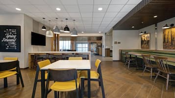Un espace de repas moderne avec des tables et des chaises, une cuisine en arrière-plan et un grand tableau accroché au mur.