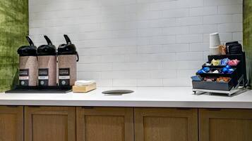 A coffee station with three coffee dispensers labeled 'Hot Water,' 'Medium,' and 'Bold.' There are also stacks of disposable cups and a tray with various items.