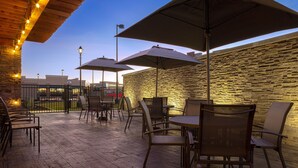 Un patio al aire libre con piso de madera, paredes de piedra y sillas y mesas de metal.