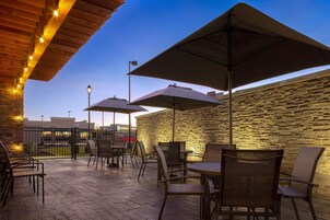 Un patio al aire libre con piso de madera, paredes de piedra y sillas y mesas de metal.