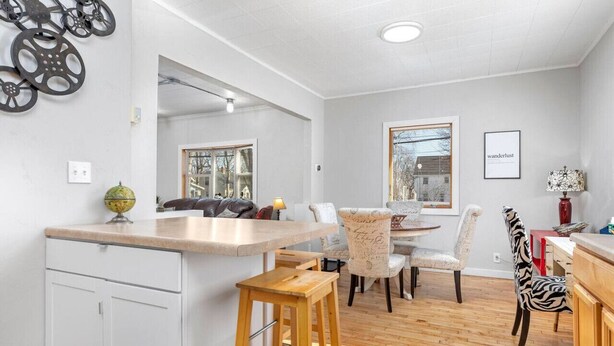 A modern kitchen with a central island, bar stools, and a dining area with patterned chairs. - Stylish, Spacious Home: Walk Downtown, Fenced Yard on Washington St. (Appleton)
