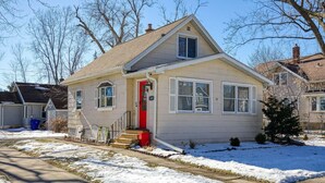 A single-story house with a red door, a front porch, and a small front yard. - Stylish, Spacious Home: Walk Downtown, Fenced Yard on Washington St. (Appleton)