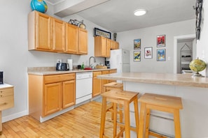 A compact kitchen with wooden cabinets, a white dishwasher, and a small island with stools.