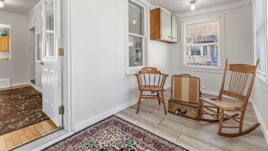 A room with a wooden floor, white walls, a patterned rug, two wooden chairs, a rocking chair, a suitcase, and a cabinet. - Stylish, Spacious Home: Walk Downtown, Fenced Yard on Washington St. (Appleton)