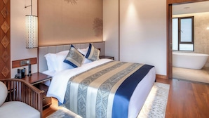 Een moderne hotelkamer met een groot bed, een nachtkastje met een lamp, een houten nachtkastje en uitzicht op een badkamer met een bad.