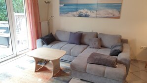 A living room with a grey sofa, a wooden coffee table, and a large ocean view painting on the wall.