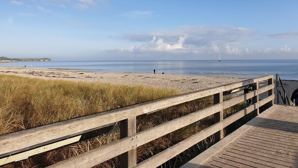 A wooden boardwalk leading to a beach with a clear view of the sea and distant land.