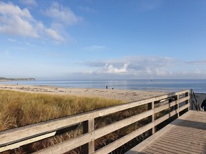 Un paseo marítimo de madera que conduce a una playa, con vistas claras al mar y a la costa distante.