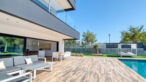 Un espace de vie extérieur moderne comprenant une piscine, un ensemble de mobilier de salle à manger et un coin salon avec un canapé et des fauteuils.