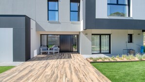 Une maison moderne à deux étages dotée d’un patio comprenant une terrasse en bois et un espace salon.