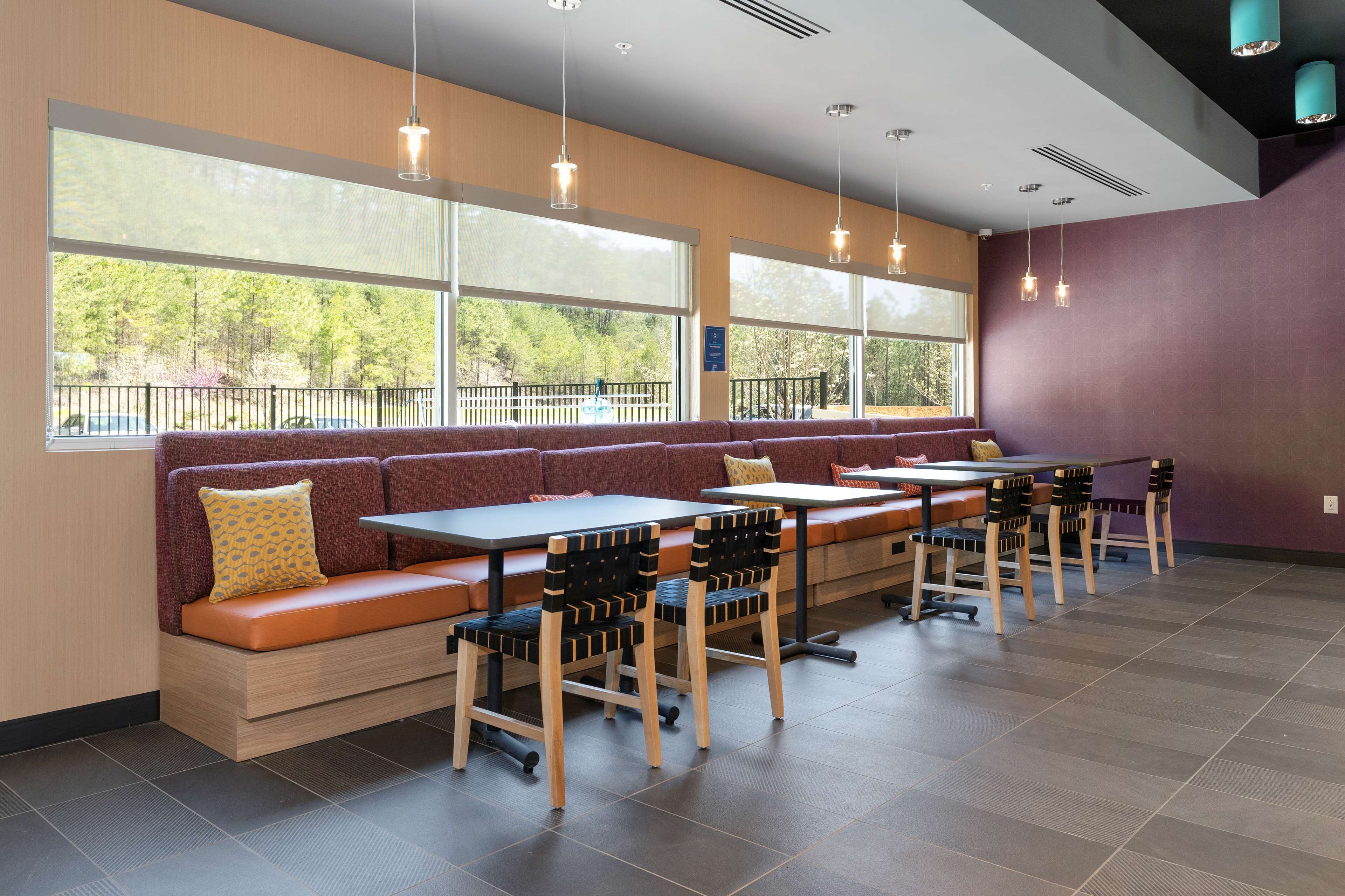 A modern restaurant with large windows, wooden tables, and cushioned seating areas.