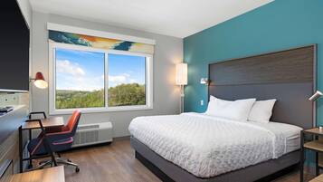 Une chambre d’hôtel moderne dotée d’un grand lit, d’un bureau, d’une chaise et offrant une vue sur l’extérieur grâce à une grande fenêtre.