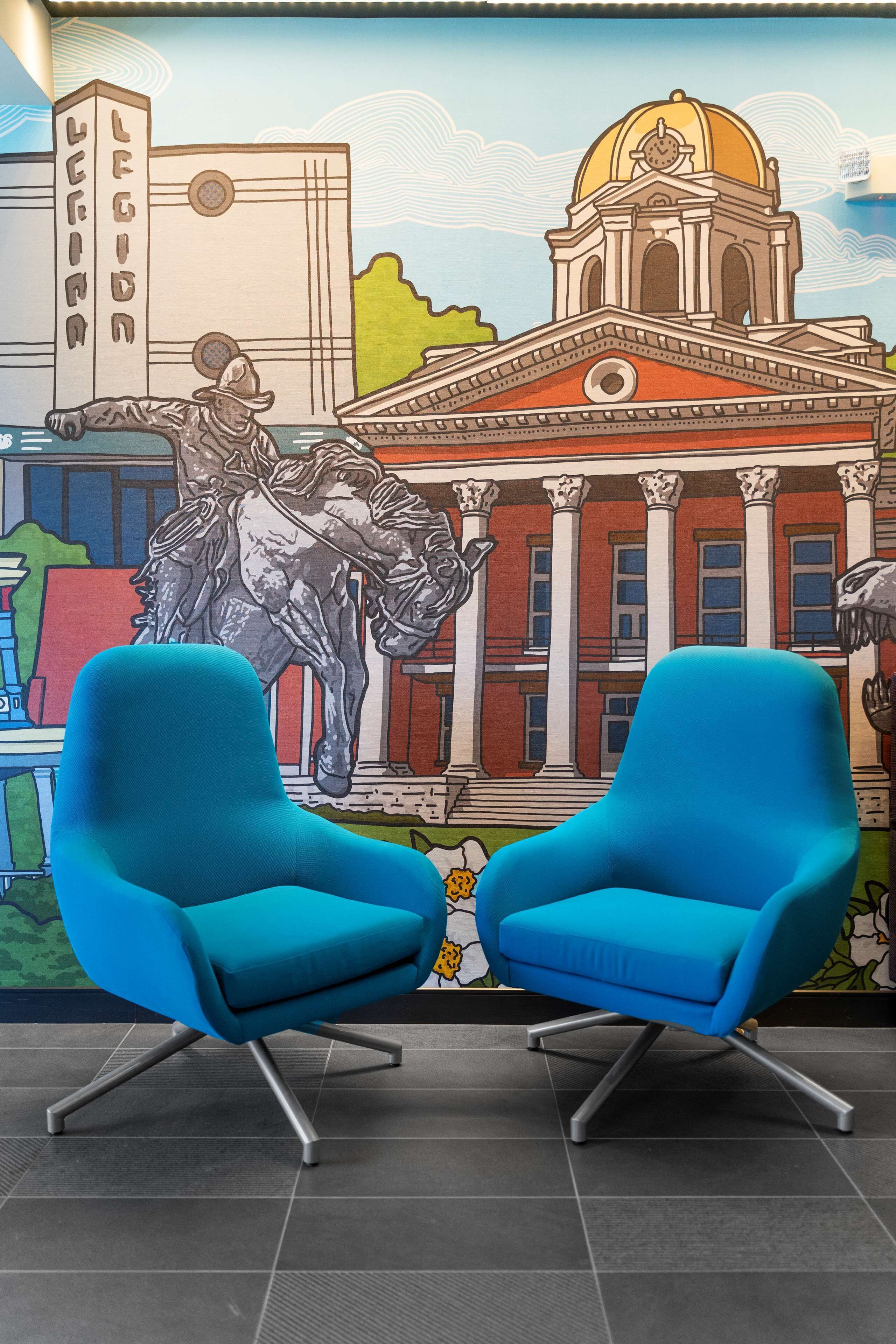 A room with two blue chairs and a mural depicting a historical building and a statue.
