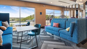 Un espace de détente moderne avec un canapé bleu, une table et des chaises, ainsi que de grandes fenêtres donnant sur l’extérieur.