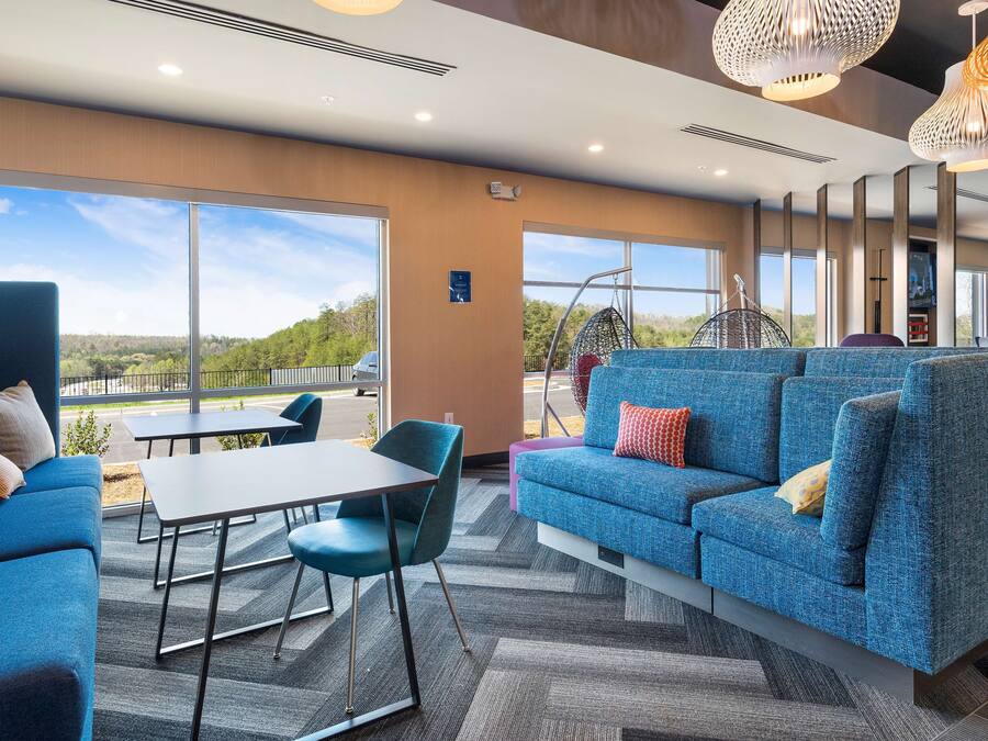 A modern lounge area with a blue sofa, a table, and chairs, large windows offering a view of the outdoors.