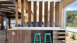Une cuisine moderne dotée d’un îlot central, de deux tabourets de bar de couleur turquoise et offrant une vue sur une forêt grâce à de grandes fenêtres.