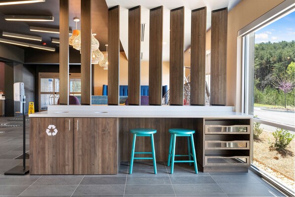 Una cocina moderna con una isla central, dos taburetes color turquesa y vistas a un bosque a través de grandes ventanales.