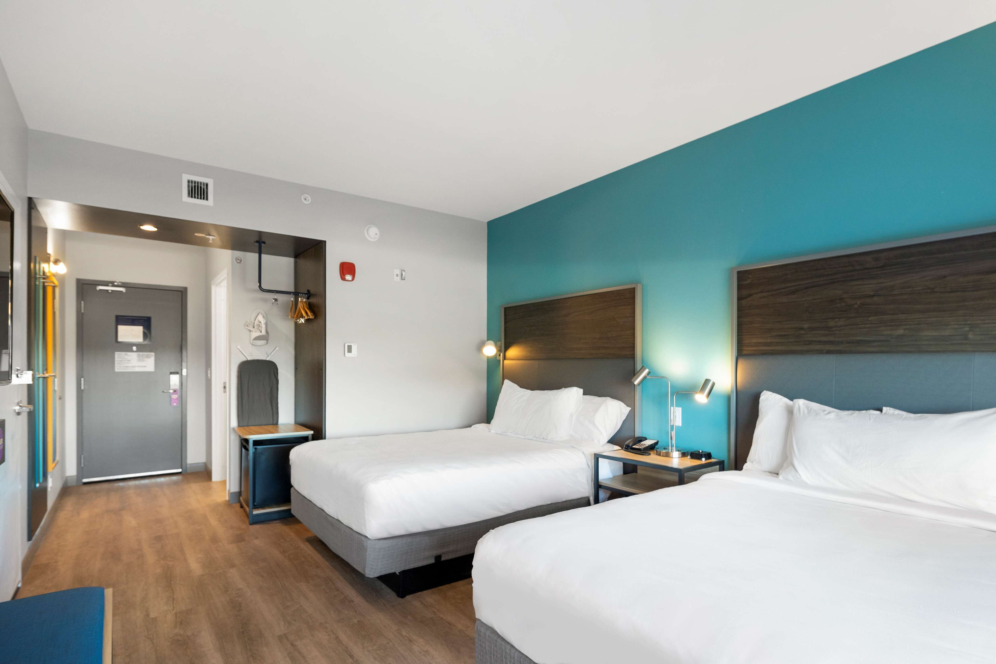 A hotel room with two beds, a desk, a chair, a wardrobe, and a bathroom.