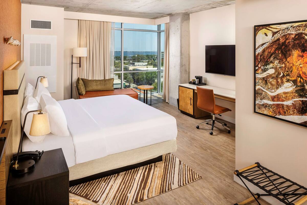 Une chambre d’hôtel avec un grand lit, un bureau, une chaise, une télévision et une fenêtre donnant sur la ville.
