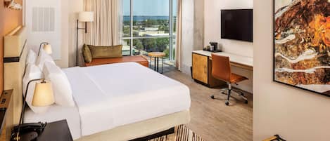 Une chambre d’hôtel avec un grand lit, un bureau, une chaise, une télévision et une fenêtre donnant sur la ville.