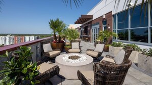 Eine Dachterrasse mit Korbmöbeln, einem Feuerkorb und Topfpflanzen.