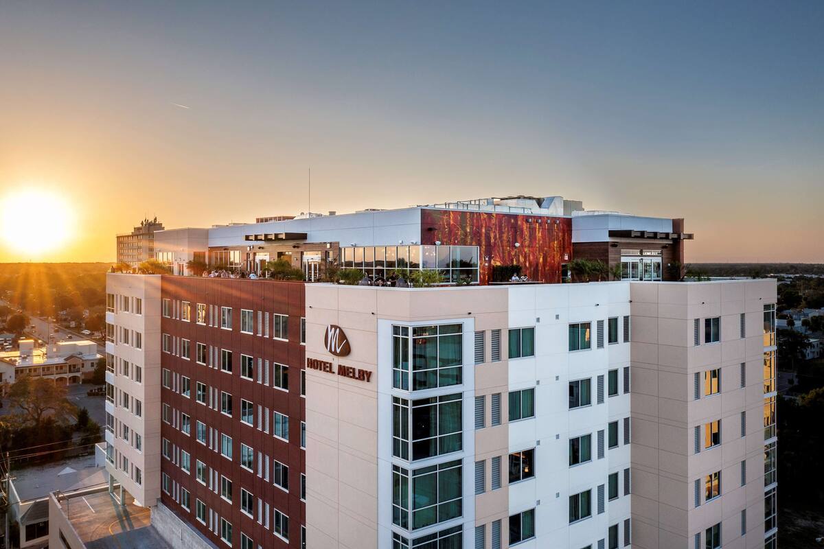 Un hôtel au design moderne, caractérisé par un mélange de façades rouges et blanches, de grandes fenêtres et une terrasse sur le toit.