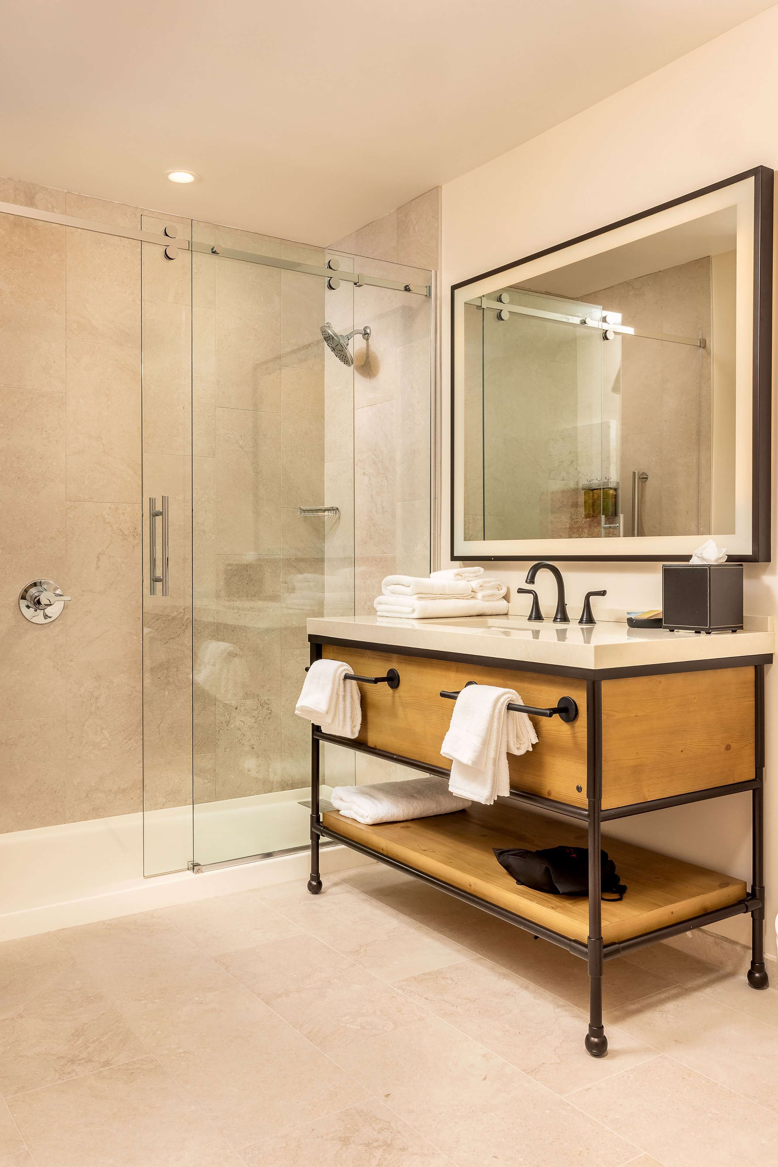 A modern bathroom with a glass-enclosed shower, a wooden vanity with a mirror, and a towel rack.