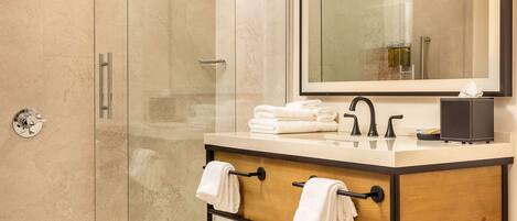 Un baño moderno con ducha envuelta en vidrio, tocador de madera con espejo y un perchero para toallas.