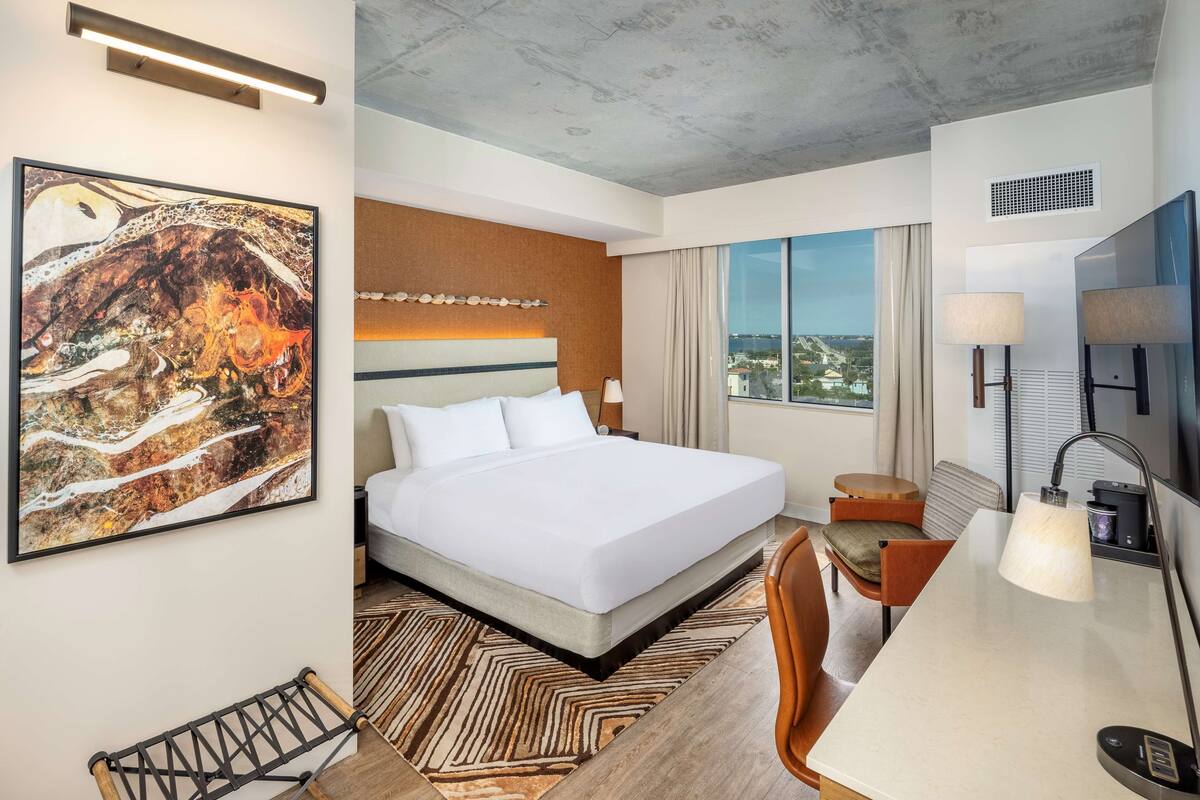 Une chambre d’hôtel avec un grand lit, un bureau, une chaise, une télévision et un tableau au mur.