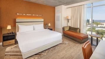 Una habitación de hotel moderna con una cama grande, un sofá, una mesita y vistas a la ciudad.