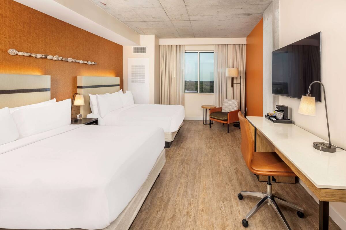 Une chambre d’hôtel avec deux lits, un bureau, une chaise, une télévision et une fenêtre avec des rideaux.