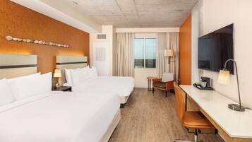 A hotel room with two beds, a desk, a chair, a TV, and a window with curtains.