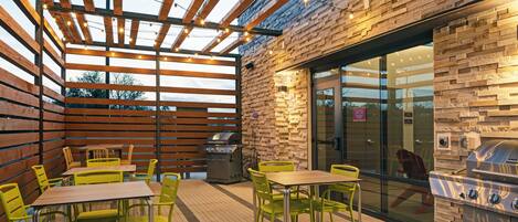 Une terrasse extérieure avec des tables et des chaises en bois, un barbecue et un mur en briques.