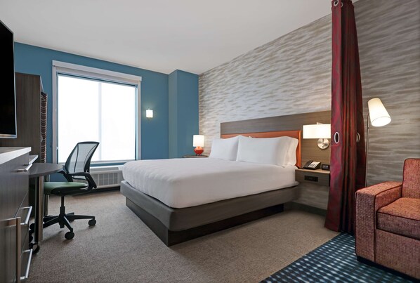 Una habitación de hotel con cama, escritorio, silla y un ventanal grande.