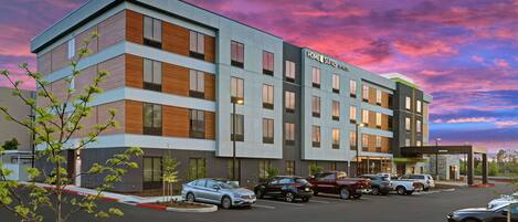 A modern hotel with a multi-story structure, a parking lot, and a clear sky.