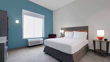 A hotel room with a large bed, a window, a heater, a desk, and a lamp.