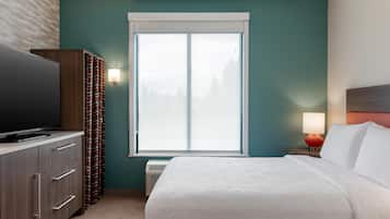 Habitación de hotel con una cama grande, un televisor sobre un mueble de madera, una ventana con cortinas y una mesita de noche con lámpara.