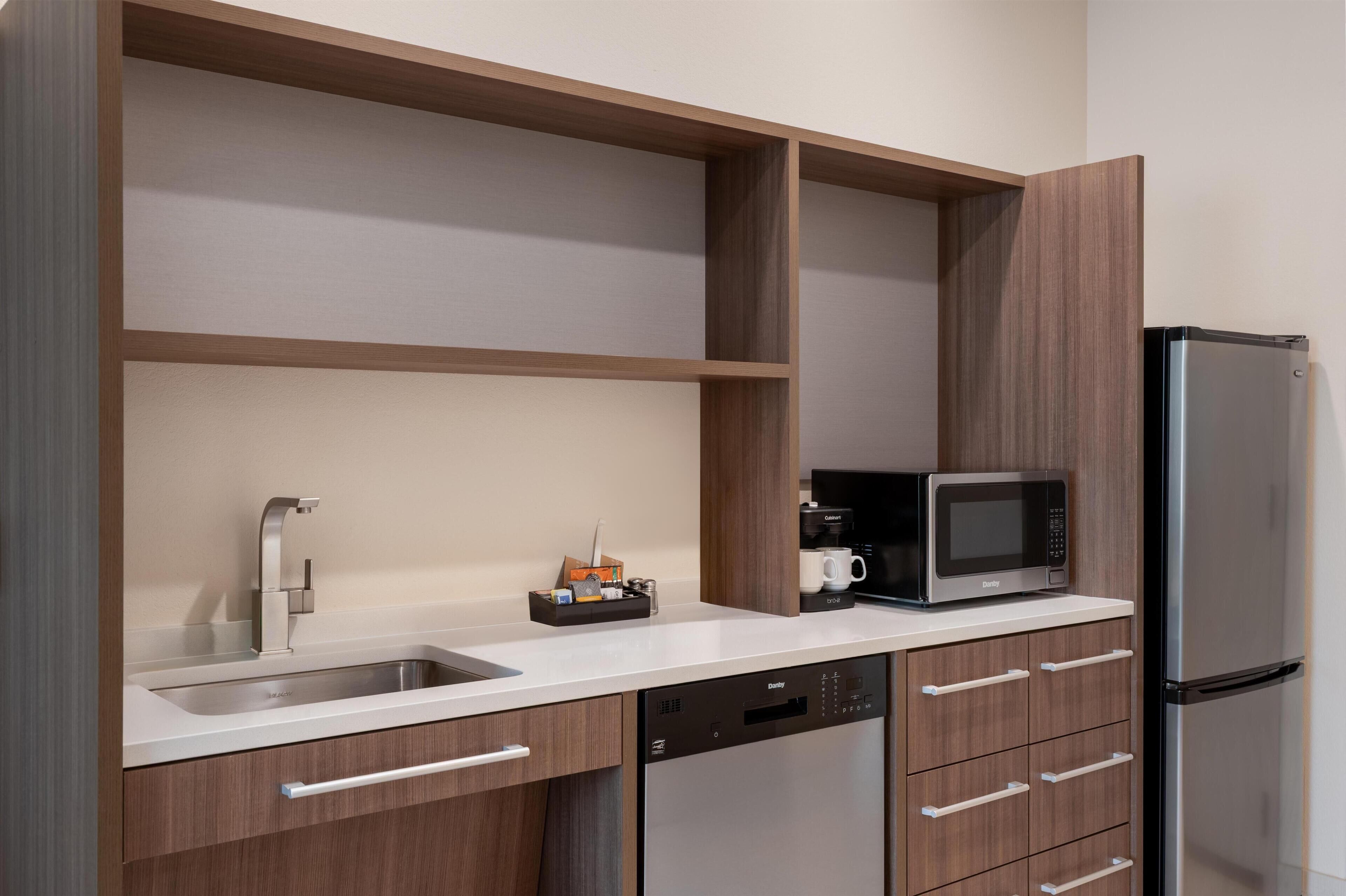 A modern kitchen with a stainless steel refrigerator, a built-in microwave, a coffee maker, and a dishwasher.