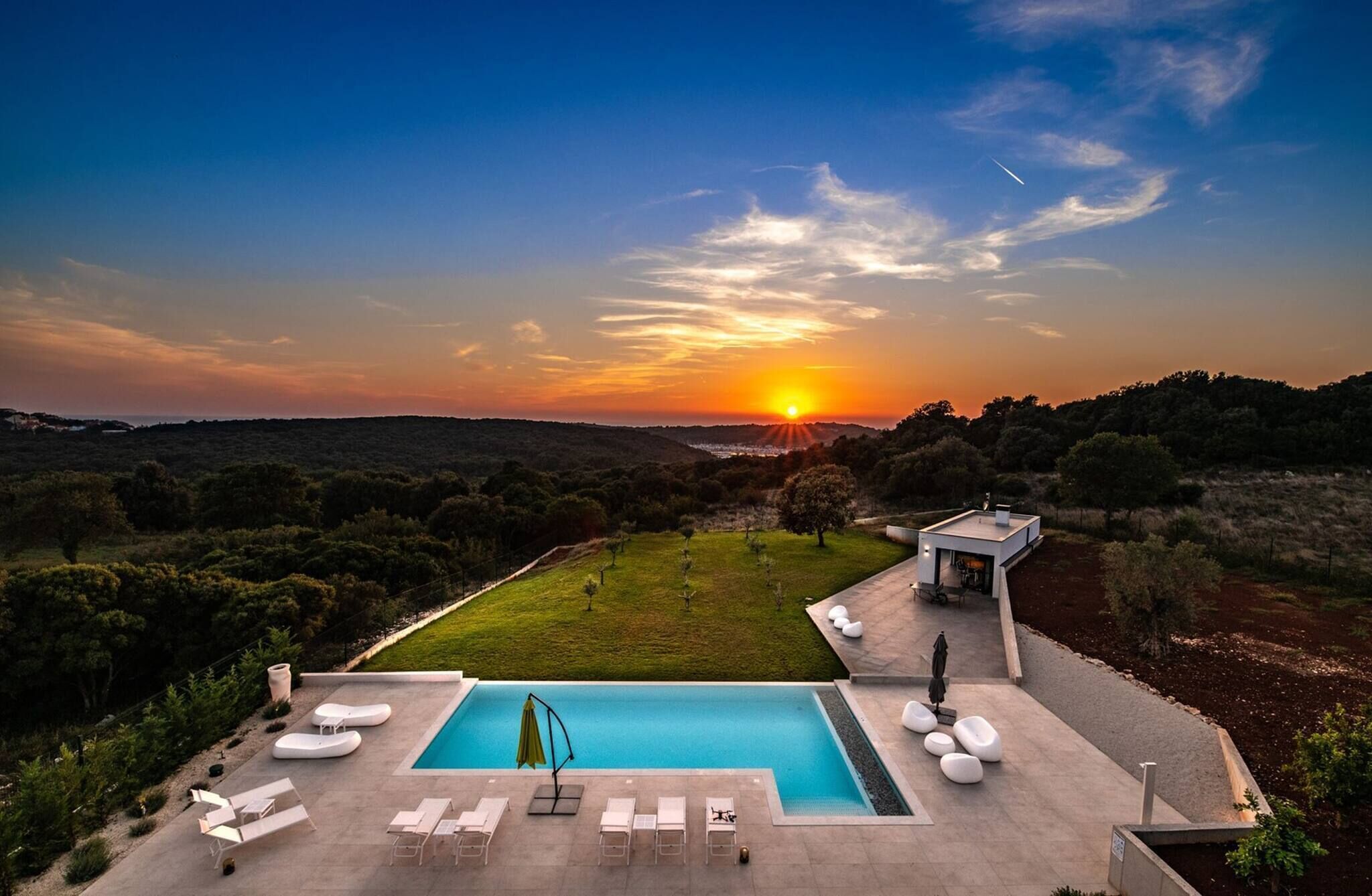 A pool area with lounge chairs and a small building, surrounded by a landscaped garden and a view of the sunset.