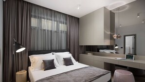 A modern bedroom with a large bed, bedside lamp, bedside table, and a mirror above the desk.