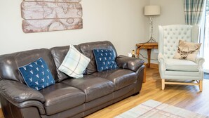 Een woonkamer met een bruine leren bank, een witte fauteuil en een wereldkaart op de muur.